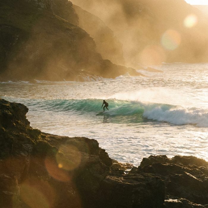 Business Motivation: Steilküste im Morgenlicht mit einem Surfer im Wasser
